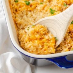Close-up of cheesy chicken and rice casserole being scooped from a blue-rimmed baking dish.