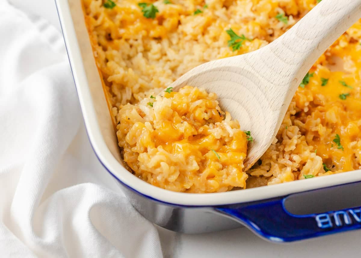 This easy chicken and rice casserole is a quick and delicious dinner idea that the whole family will love. It's made with just 4 simple ingredients...most of which you probably already have in your pantry! Close-up of cheesy chicken and rice casserole being scooped from a blue-rimmed baking dish.