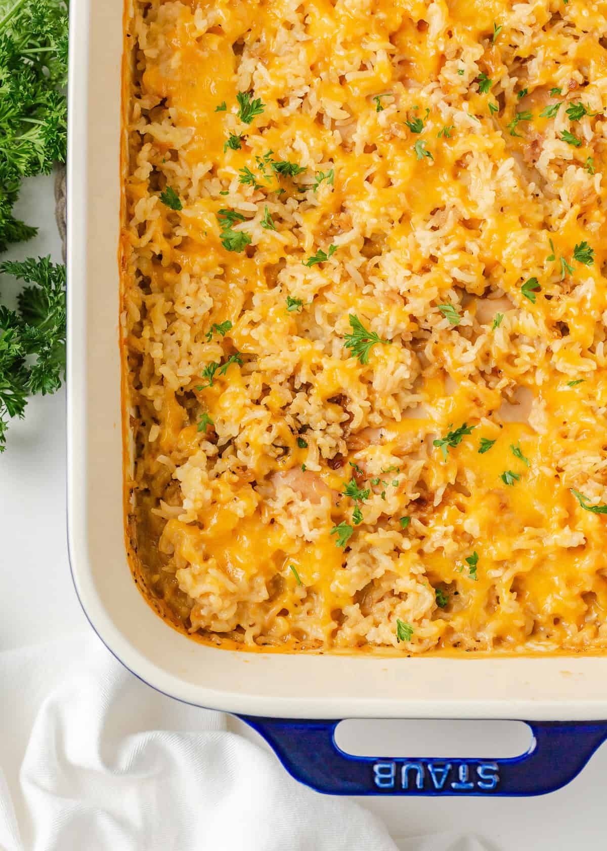 This easy chicken and rice casserole is a quick and delicious dinner idea that the whole family will love. It's made with just 4 simple ingredients...most of which you probably already have in your pantry! Overhead view of one pan chicken and rice casserole topped with parsley in a white baking dish.