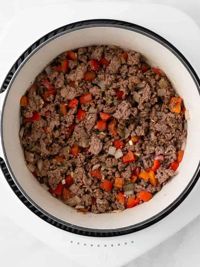 Ground beef, onion and pepper in a white pot.