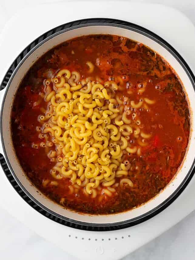Elbow noodles and tomato sauce added to a pot containing beef and veggies.