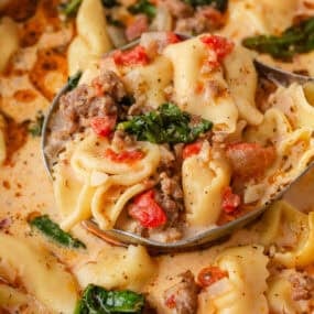 Ladle filled with creamy Tuscan tortellini soup, sausage, spinach and tomatoes.