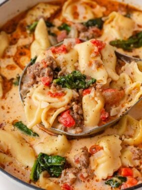 Ladle filled with creamy Tuscan tortellini soup, sausage, spinach and tomatoes.