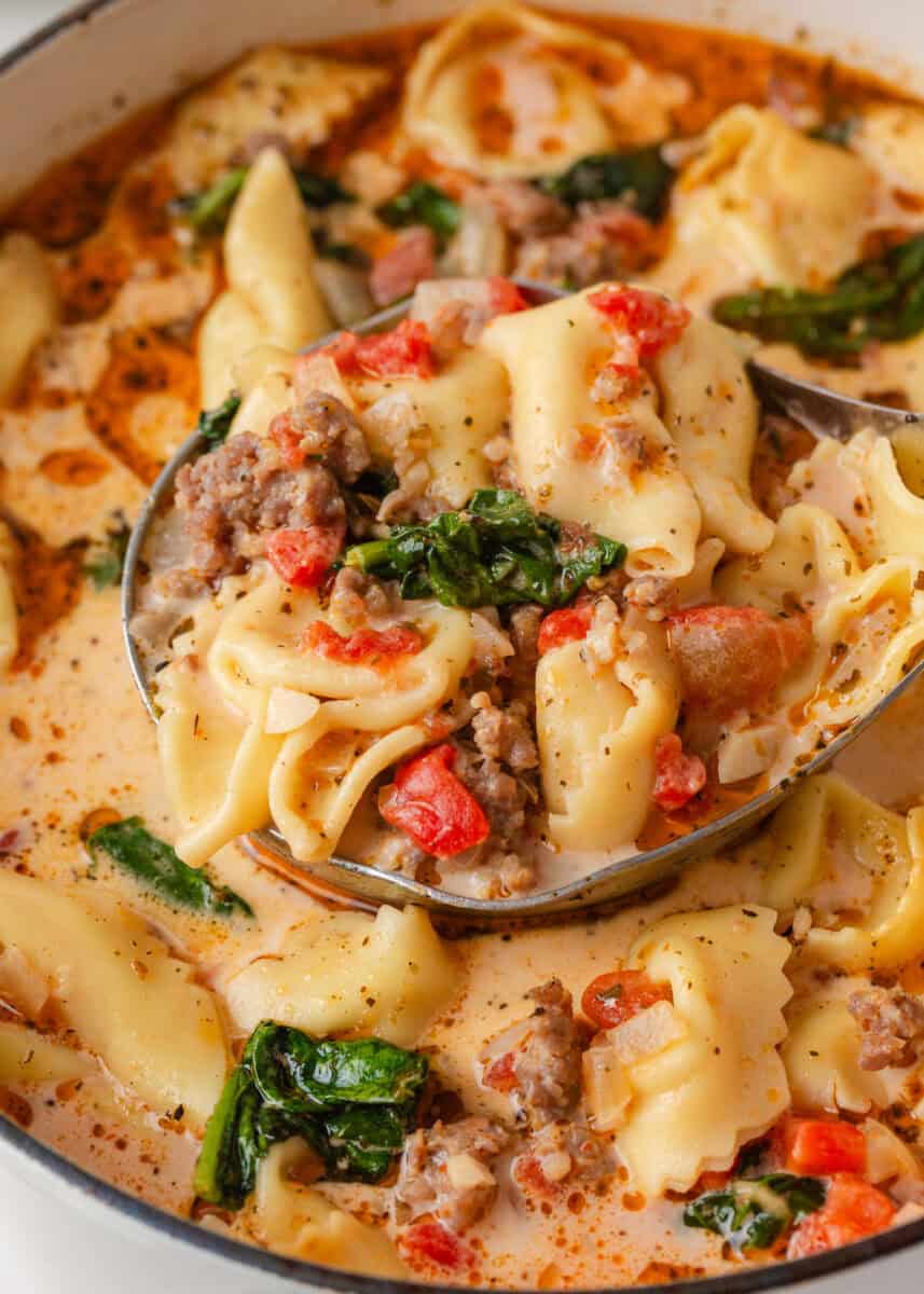Ladle filled with creamy Tuscan tortellini soup, sausage, spinach and tomatoes.