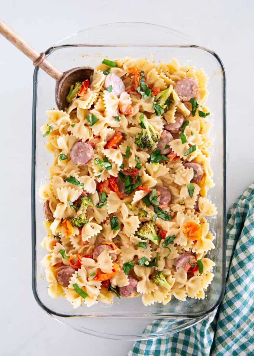 Overhead view of a baking dish of Boursin cheese pasta with farfalle, sausage, broccoli and fresh basil.