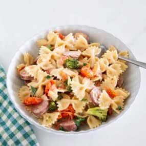 Overhead view of creamy Boursin cheese pasta with sausage, broccoli and tomatoes in a glass baking dish.
