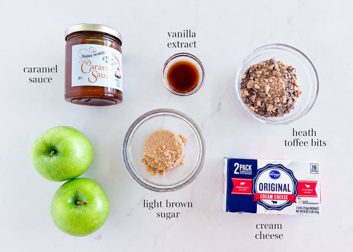 Caramel apple cheesecake dip ingredients including cream cheese, brown sugar, vanilla, caramel sauce, toffee bits and green apples.