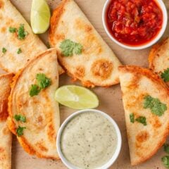 Overhead view of crispy chicken tacos served with salsa, creamy sauce, cilantro and lime wedges.