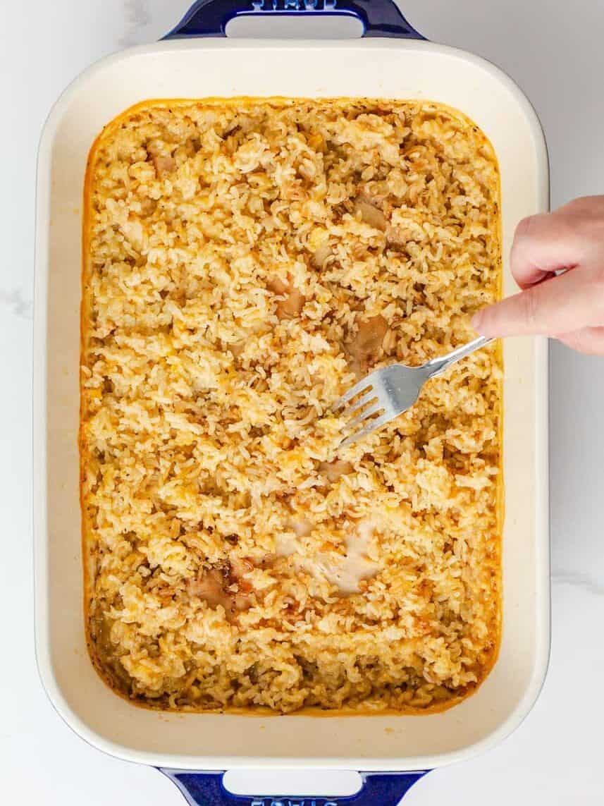 Baked chicken and rice casserole as a fork loosens the rice around the chicken.
