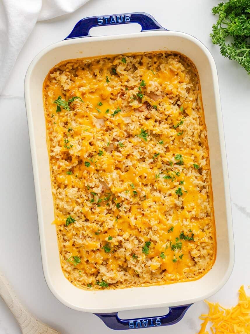 Cheesy chicken and rice casserole topped with parsley in a white baking dish.