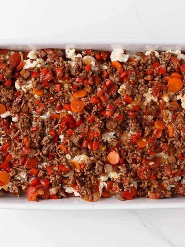 Ground beef and tomato mixture layered over creamy elbow macaroni in a casserole dish.