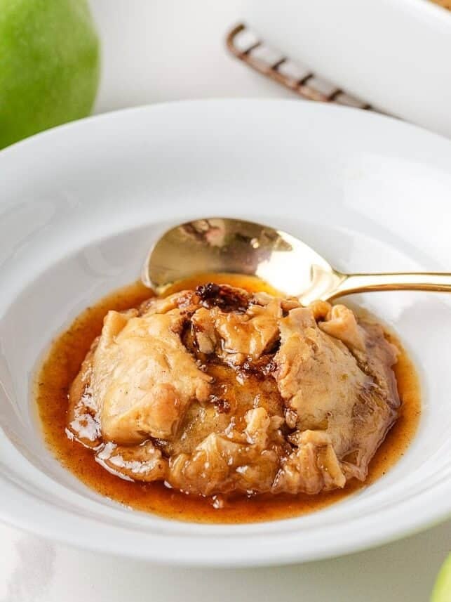 Single serving of old fashioned apple dumpling in a white bowl with golden syrup, ready to eat with a spoon.