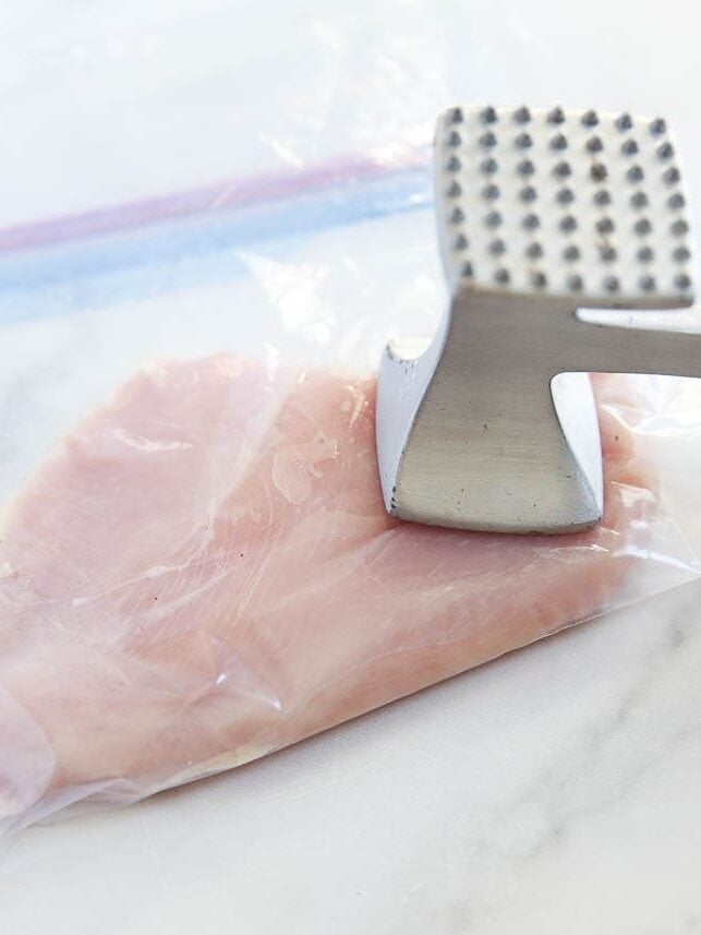 Pounding chicken breast to even thickness with a meat mallet in a zip top bag.