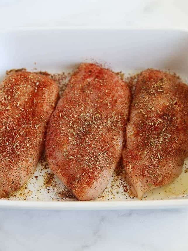 Seasoned chicken breasts in a white baking dish ready to go in the oven.