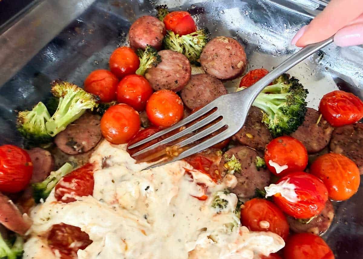 Fork stirring softened Boursin cheese into roasted sausage, broccoli and tomatoes.