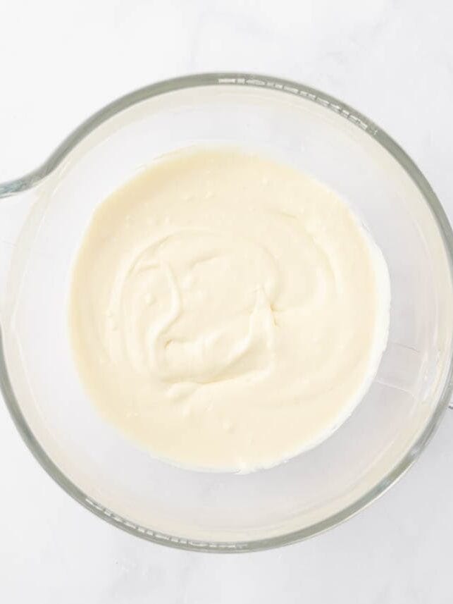 Creamy cheesecake cake bar filling in a glass measuring cup.