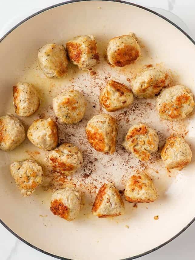 Chicken meatballs browning in a large white skillet.