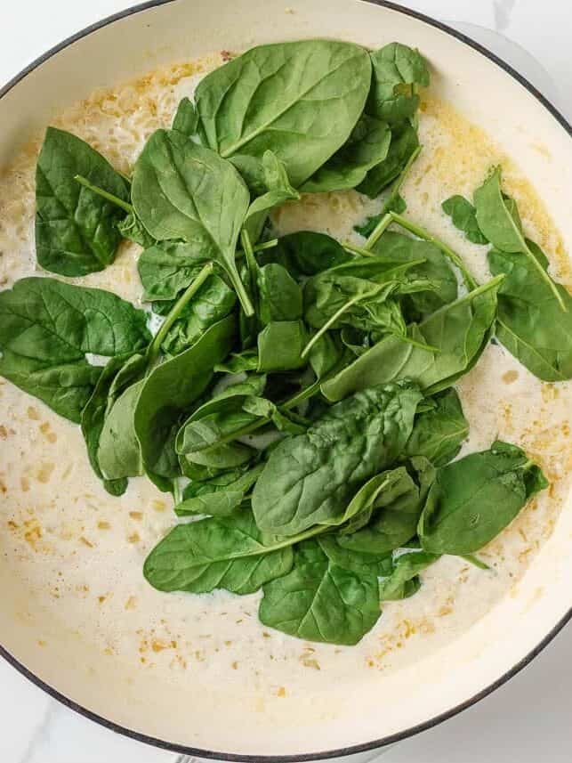 Fresh baby spinach added to creamy orzo in a skillet.