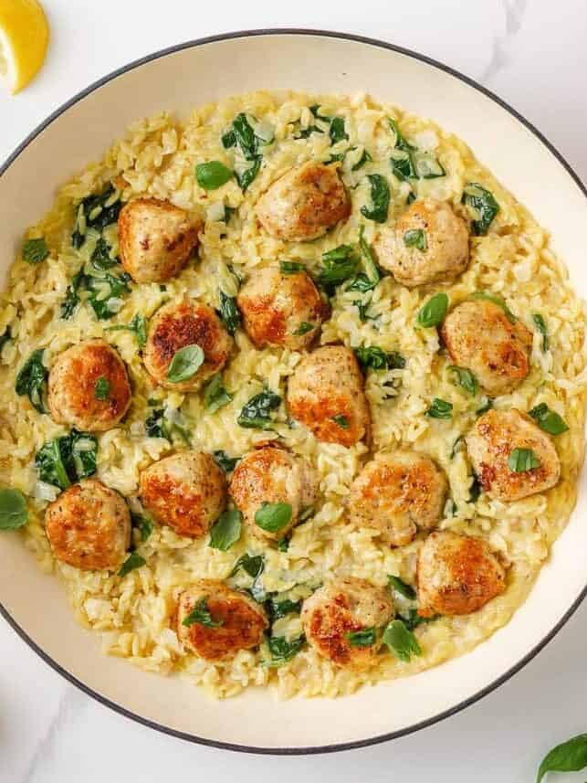Creamy chicken meatballs with orzo and spinach in a white skillet.