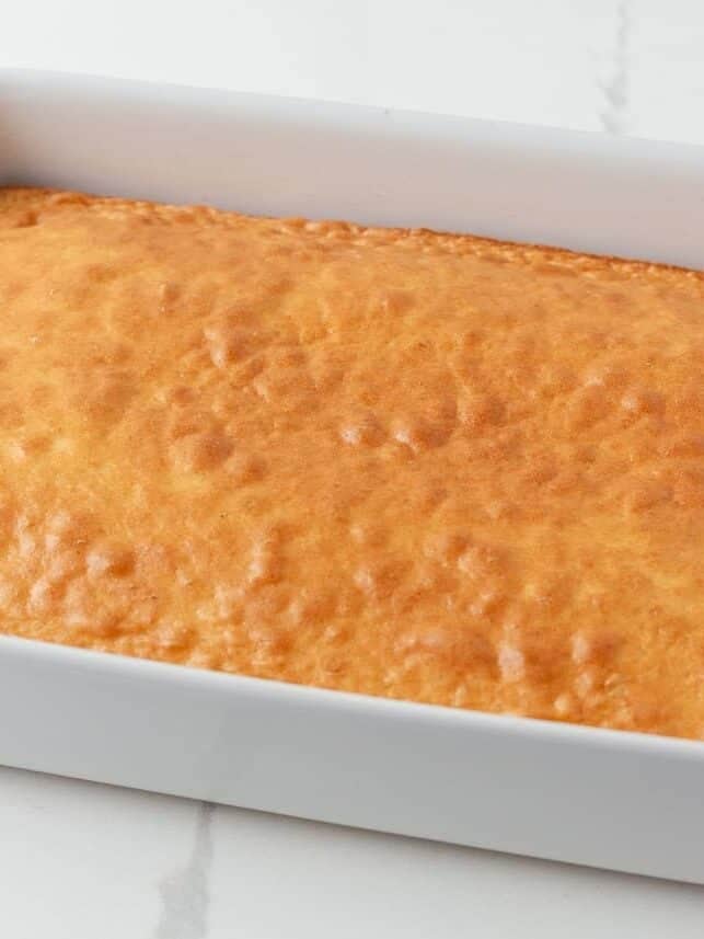 Baked vanilla cake cooling in a white 9x13-inch baking dish.