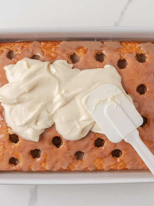 Spreading cream cheese frosting over cinnamon roll poke cake.