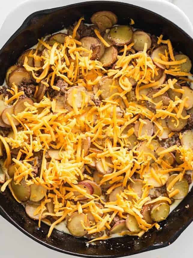 Cheddar cheese melting over ground beef and potatoes in a skillet.
