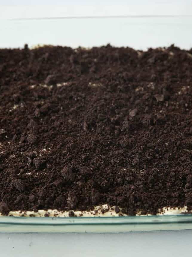 Crushed Oreo crumbs covering the creamy pudding filling in a glass baking dish before adding Halloween dirt cake decorations.