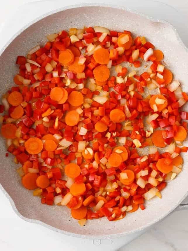 Diced bell pepper, onion and carrots sautéing in a skillet.