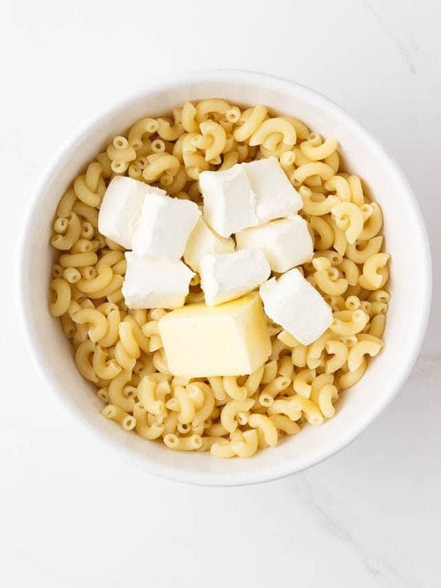 Cooked elbow macaroni with cream cheese and butter in a bowl.