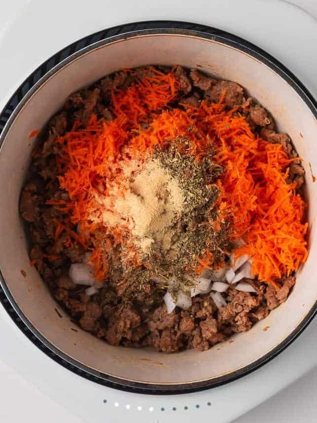 Sautéed ground sausage mixed with grated carrots, onions, and seasonings in a white pot.