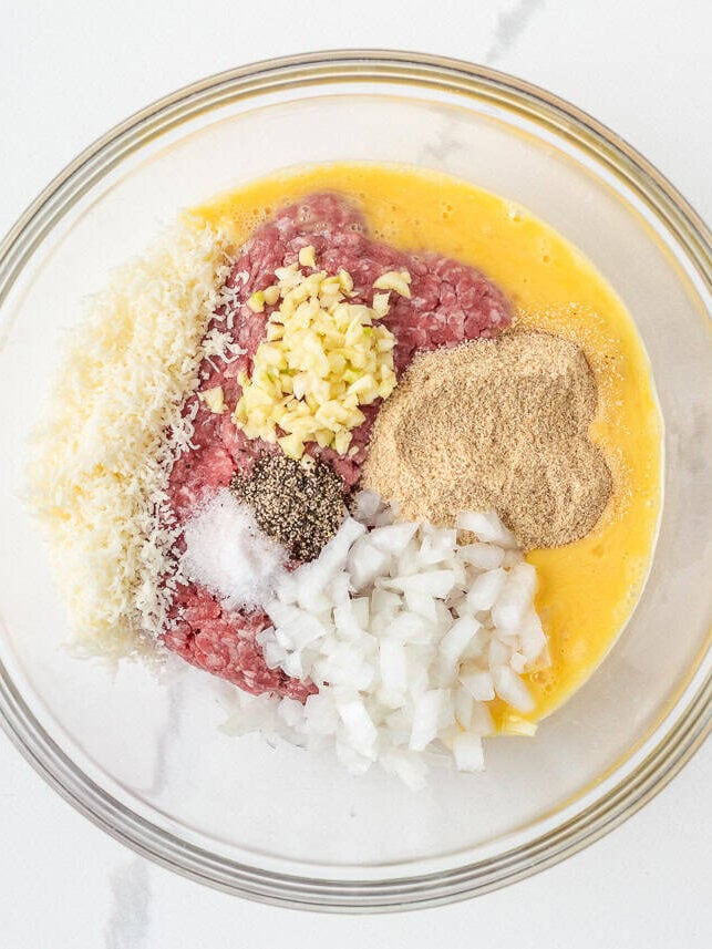 Ground beef, breadcrumbs, Parmesan, onion, garlic, egg and seasonings in a glass bowl for making meatballs.