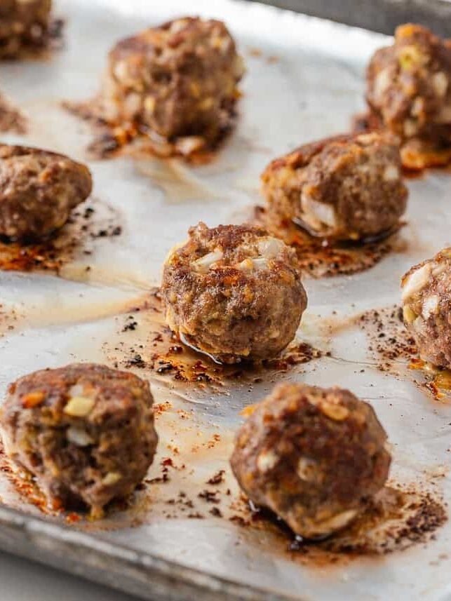 Homemade beef meatballs baked until browned on a foil-lined baking sheet.