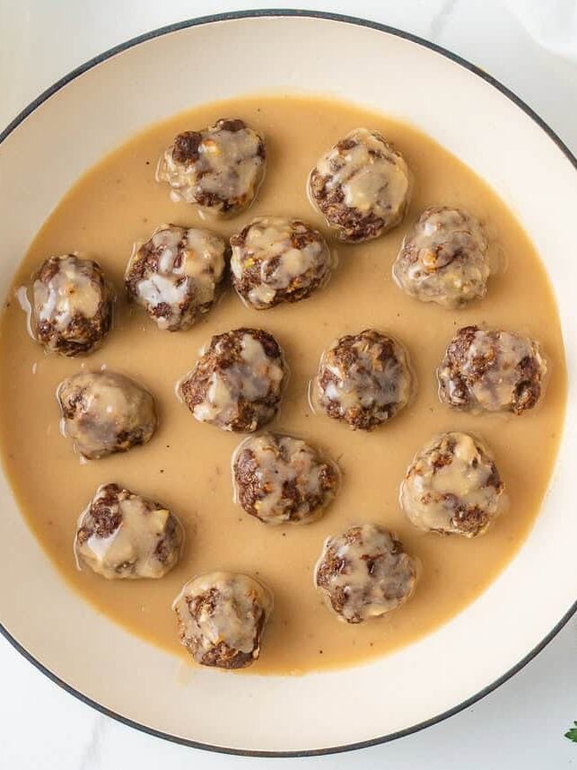 Baked meatballs added to homemade brown gravy in a skillet.