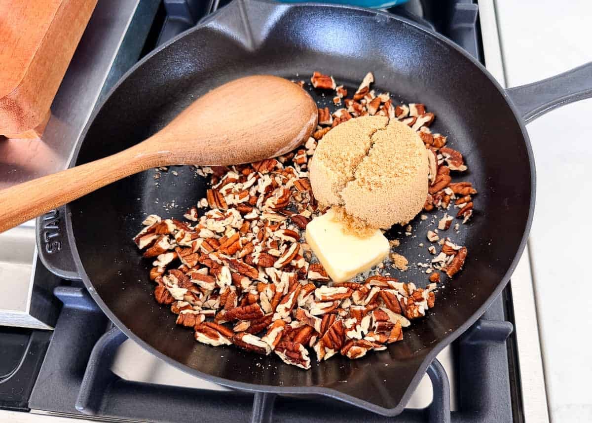 Chopped pecans toasting in a skillet with butter and brown sugar.