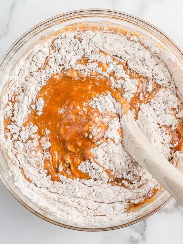 Pumpkin cake batter being mixed with the dry ingredients in a glass bowl.