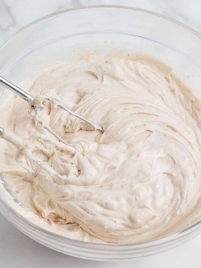 Spiced cream cheese frosting being whipped with an electric mixer in a glass bowl.