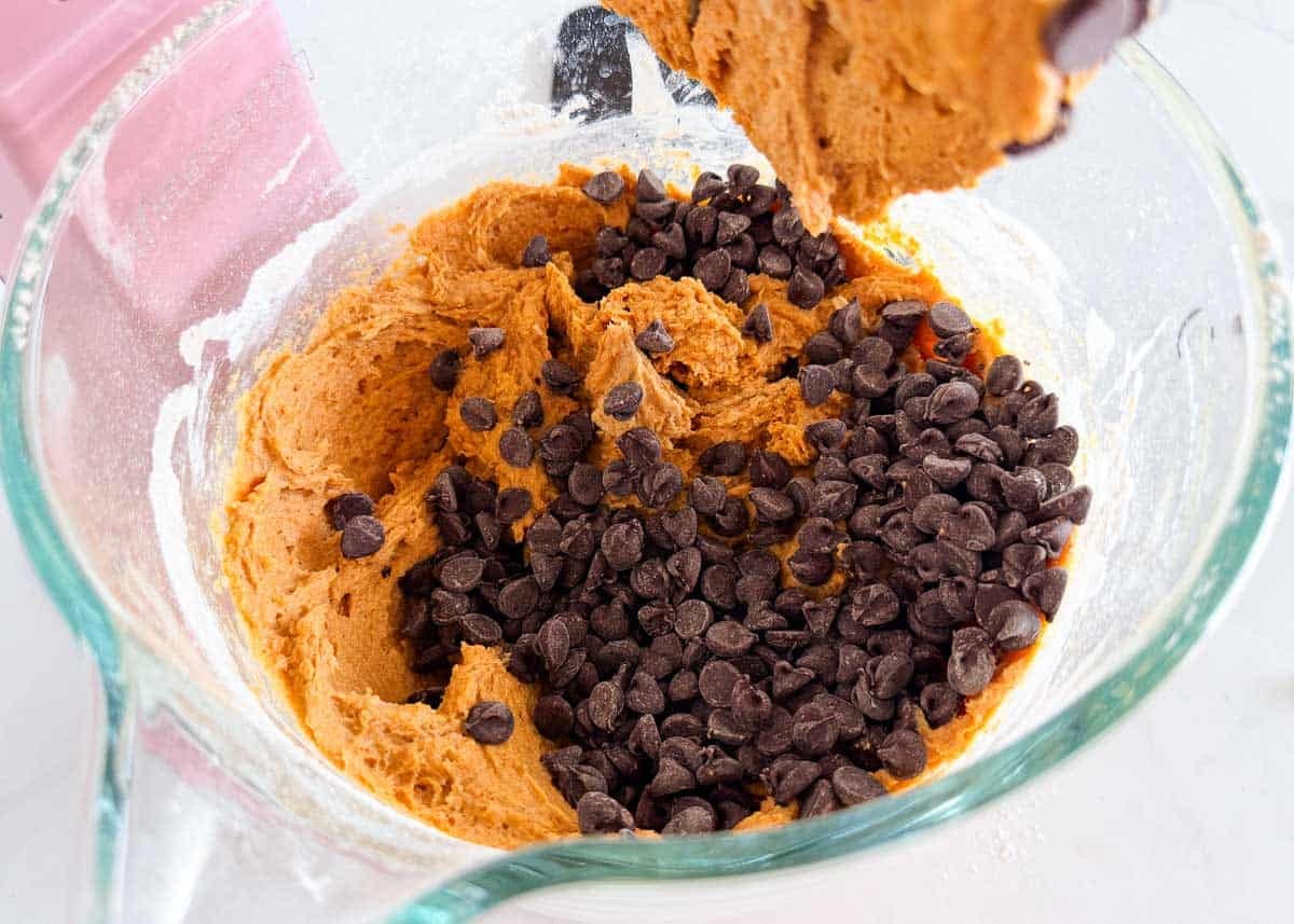 Pumpkin cake batter with chocolate chips being folded in with a spatula.
