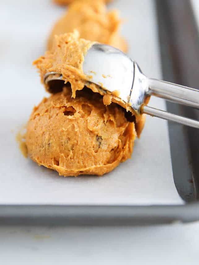 Pumpkin cake mix cookie batter being scooped onto a baking sheet.