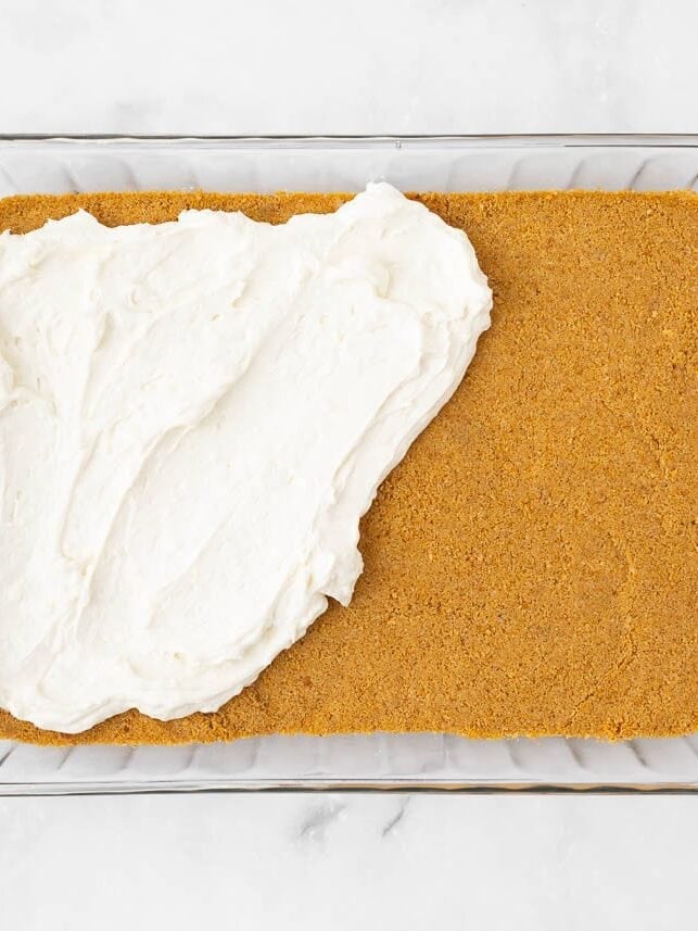 Spreading cream cheese filling over the baked graham cracker crust.