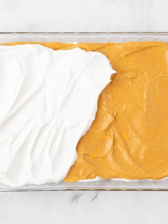 Spreading whipped topping over the pumpkin layer of the dessert lasagna.
