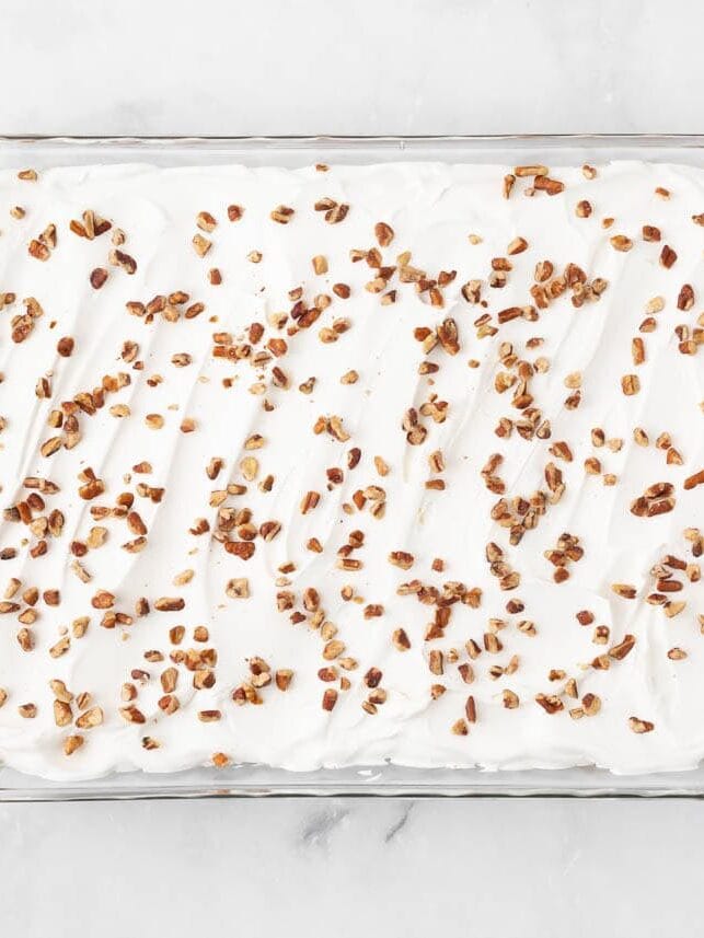 Finished pumpkin lasagna dessert topped with whipped cream and chopped pecans in a baking dish.