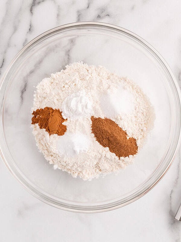 Dry ingredients for pumpkin spice cupcakes in a glass mixing bowl with warm spices and a whisk.