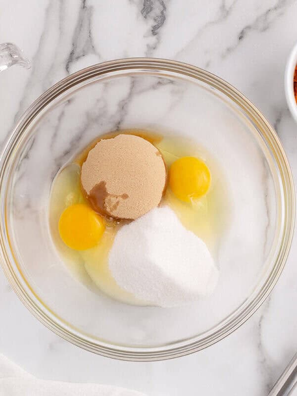 Eggs and sugars in a mixing bowl with pumpkin puree and oil ready to make pumpkin spice cupcakes.
