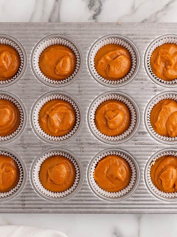 Pumpkin spice cupcake batter portioned into a lined muffin tin before baking.