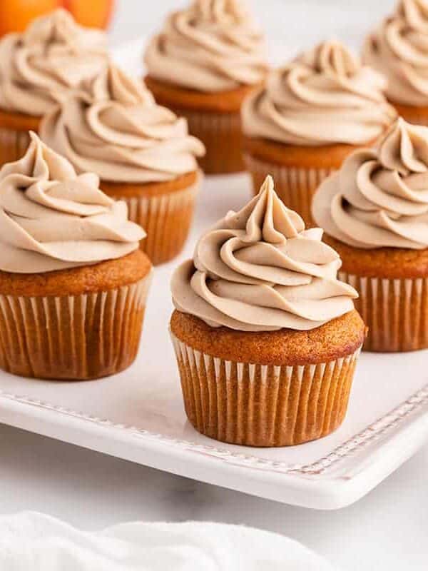 Pumpkin spice cupcakes topped with swirls of maple cream cheese frosting on a white serving platter.