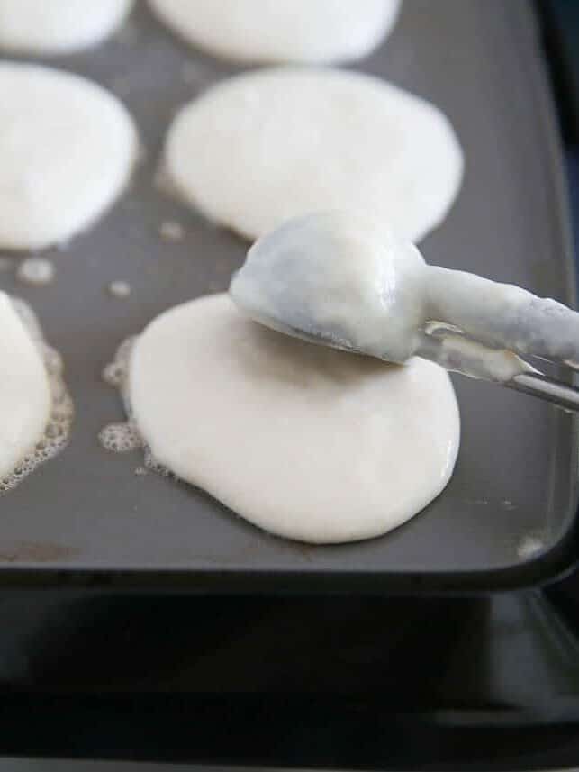 Cookie scoop with pancake batter being dropped onto a hot griddle to make silver dollar pancakes