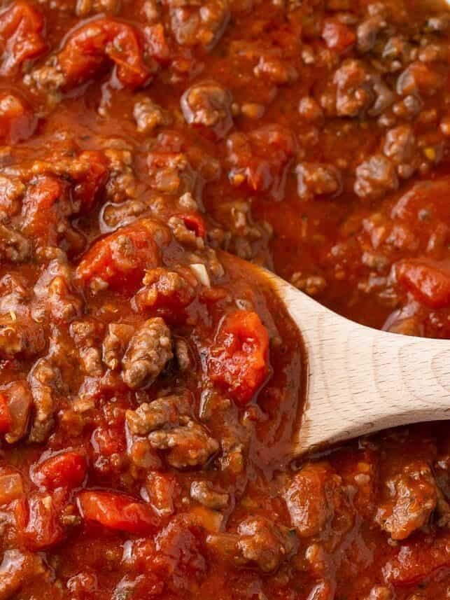 Spaghetti meat sauce simmering in a skillet with a wooden spoon.
