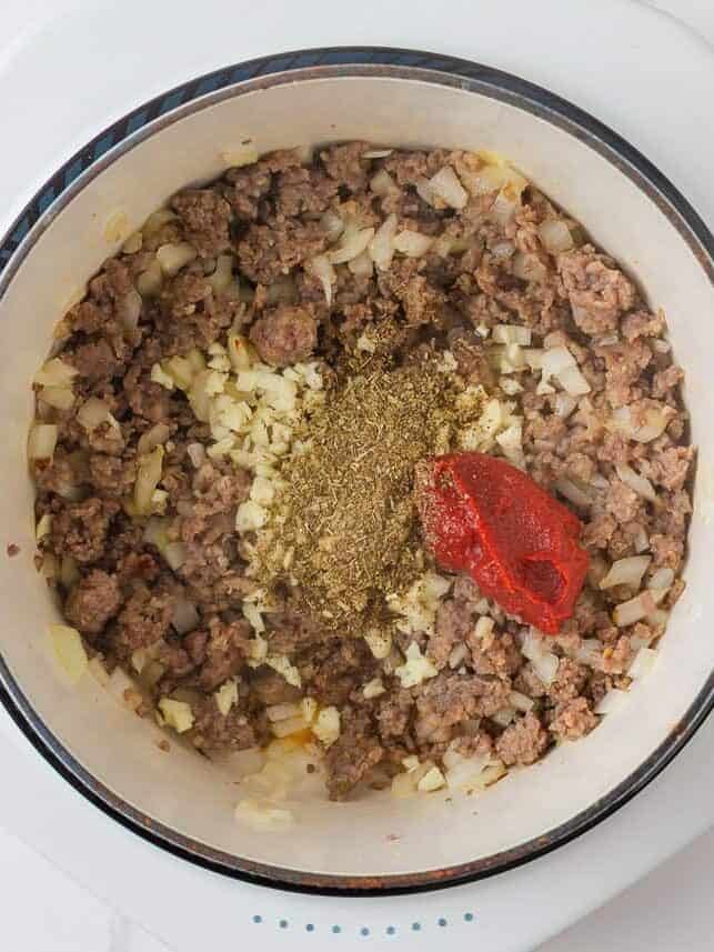 Cooked Italian sausage and onion with garlic, tomato paste and Italian seasoning in a Dutch oven.