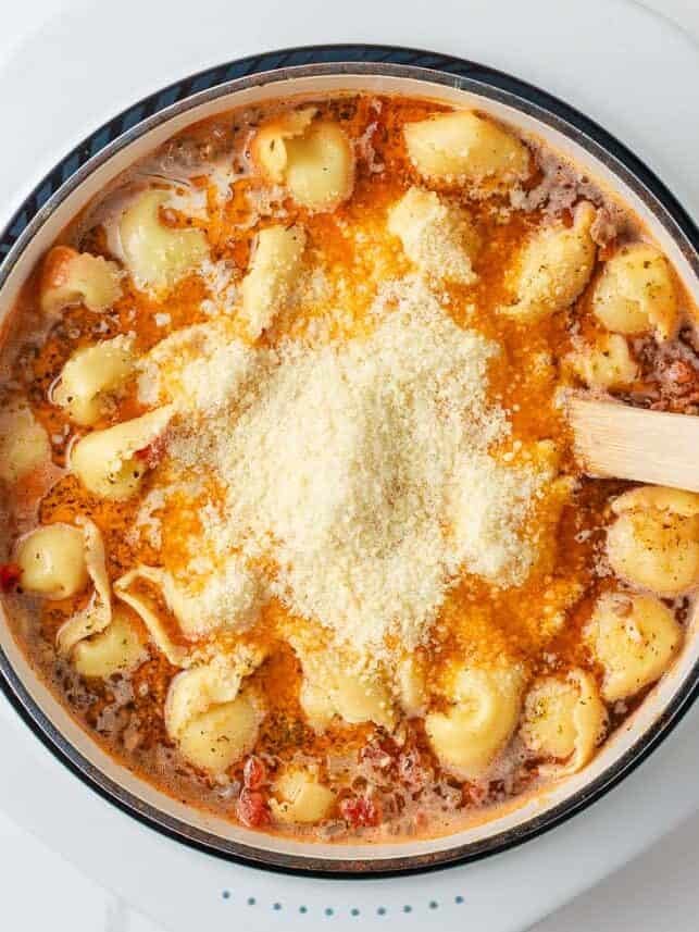 Parmesan cheese being added to creamy tuscan tortellini soup.