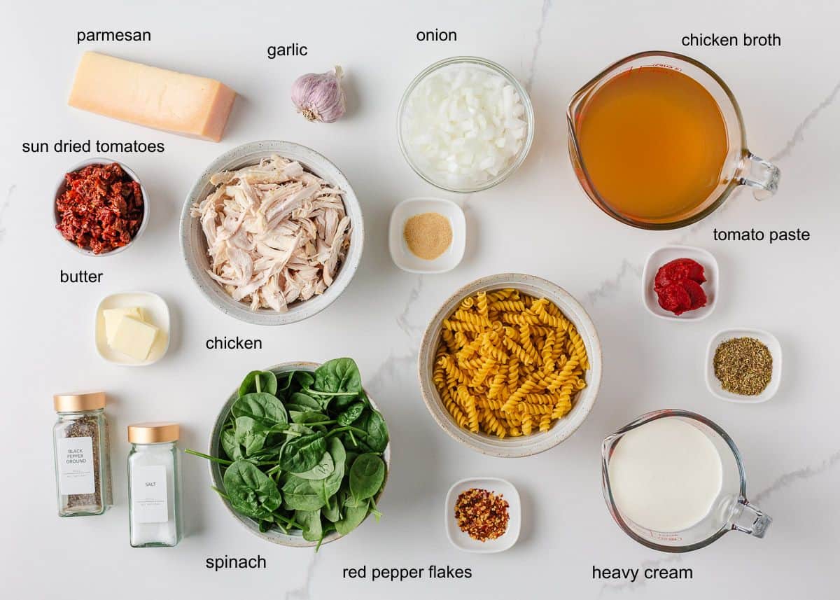 Marry me chicken soup is a cozy spin on the viral marry me chicken recipe made with tender chicken, pasta, sun-dried tomatoes and spinach in a Parmesan cream broth. Overhead view of ingredients for marry me chicken soup, including pasta, chicken, spinach, sun-dried tomatoes, onion, garlic, broth, heavy cream, and spices.